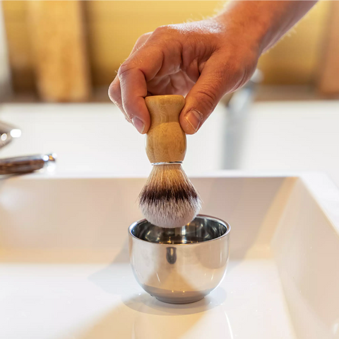 Scheerkwast wordt gebruikt in een metalen scheerbakje.