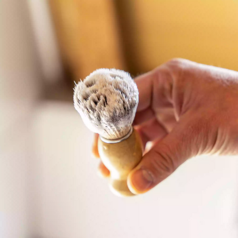 De scheerkwast met scheerzeep op de kwast in een mannenhand.