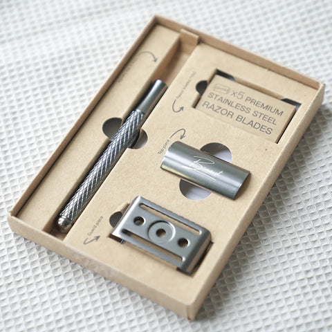 Alle onderdelen van de zwarte safety razor in het doosje, bestaande uit het handvat, top piece, guard piece en de 10 scheermesjes